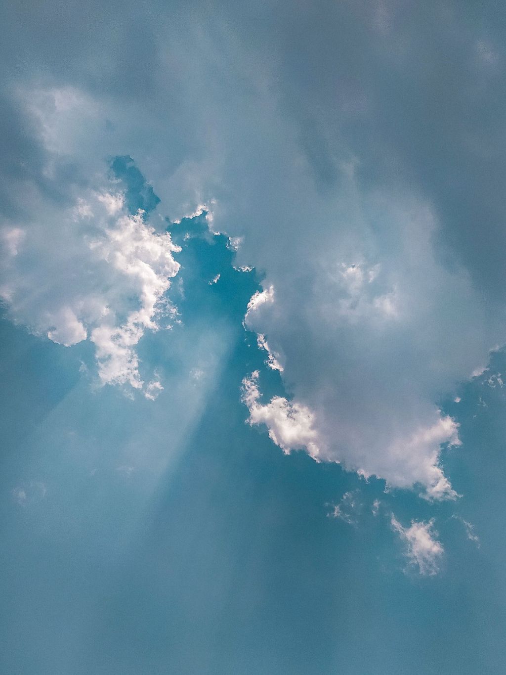 Sunlight streams through fluffy white clouds in a blue sky, creating bright rays and soft shadows across the scene.