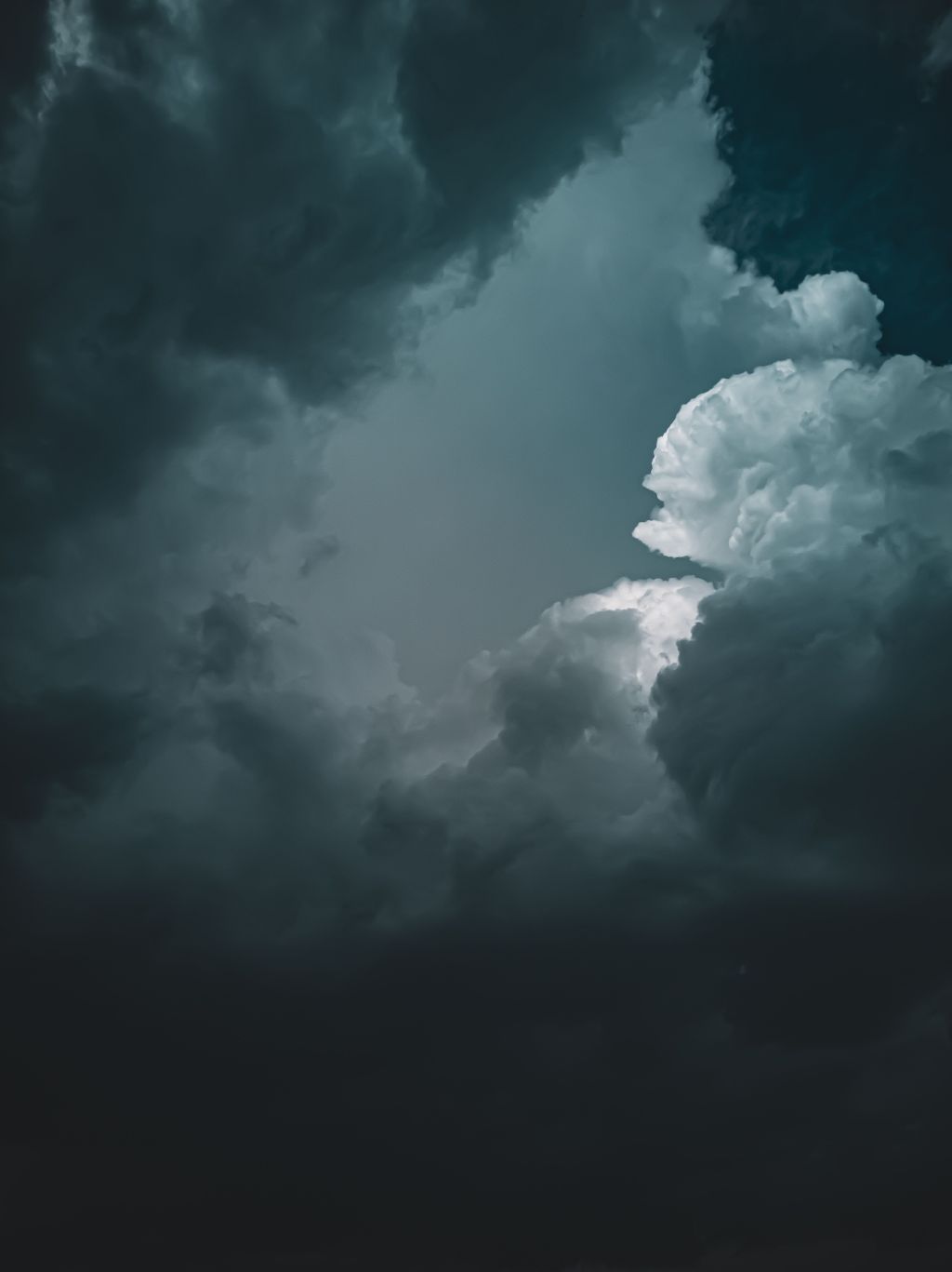 Dark, dramatic clouds with a patch of lighter sky in the center, creating a moody and intense atmosphere. The contrast between the dark and light areas highlights the cloud formations.
