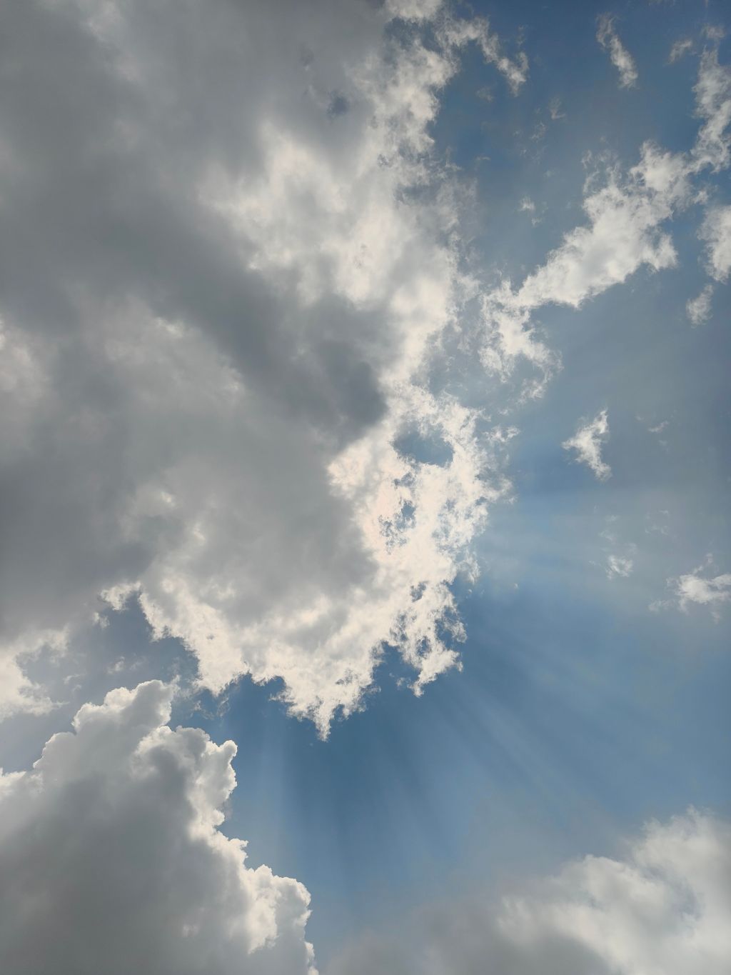 Sunlight streams through gaps in white and gray clouds in a blue sky.