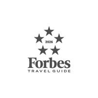 Das Logo des Forbes Travel Guide 2026 zeigt fünf in einem Kreis angeordnete Sterne über dem Schriftzug Forbes Travel Guide auf hellgrauem Hintergrund.