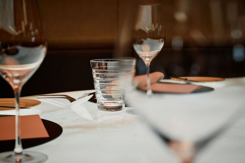 Ein Chef’s Table aus Marmor, gedeckt mit leeren Weingläsern, einem Wasserglas und Gedecken.