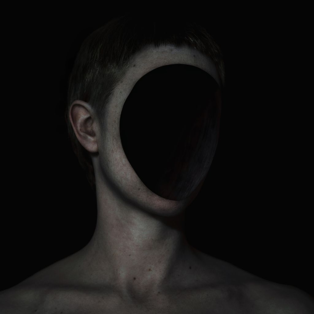 Eine Person mit kurzem Haar und nackten Schultern wird vor einem dunklen Hintergrund gezeigt. Ihr Gesicht ist vollständig verdunkelt, was ein unheimliches, gesichtsloses Aussehen erzeugt.